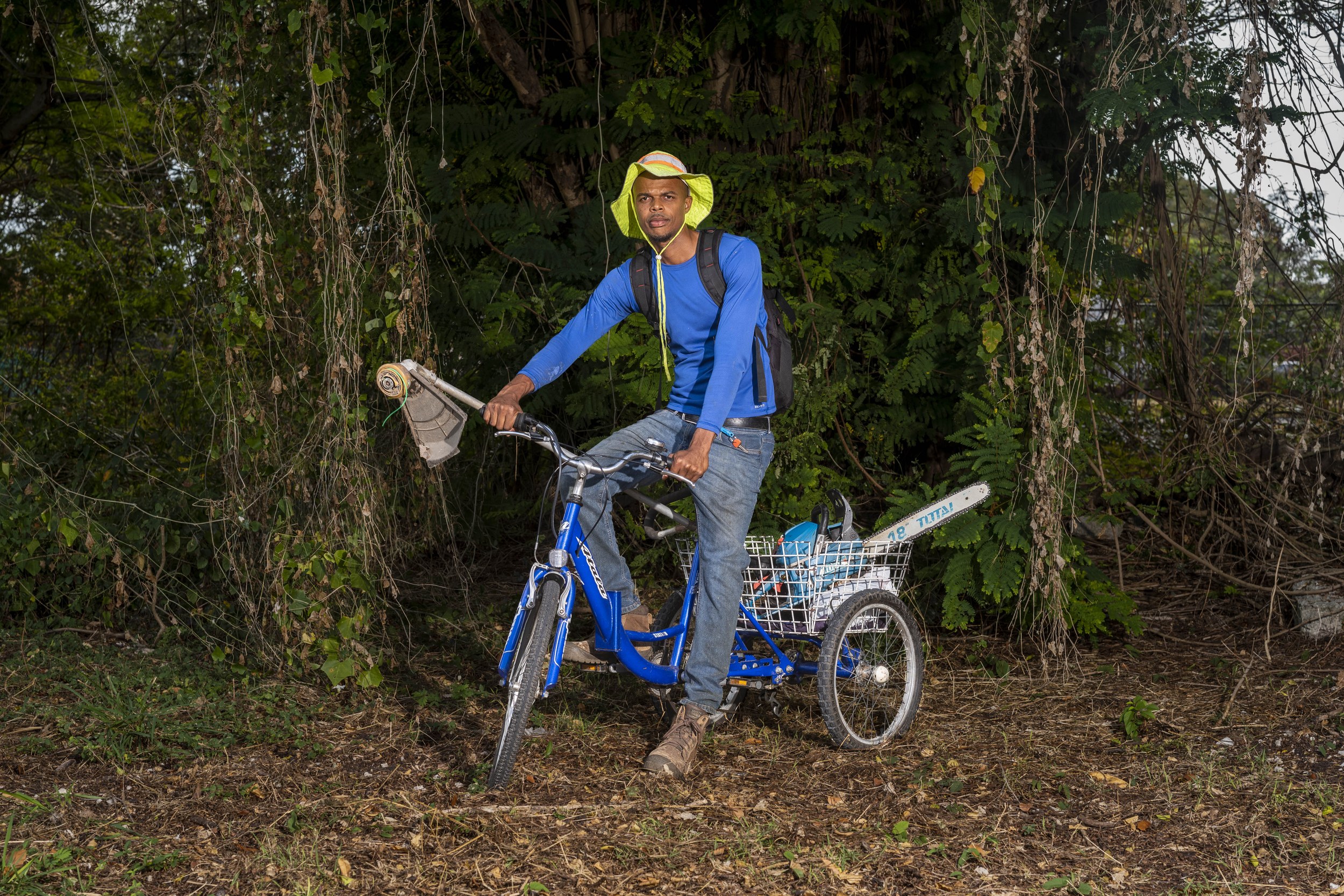 Kyle “Spider” Harewood with a bicycle and landscaping equipment in Barbados