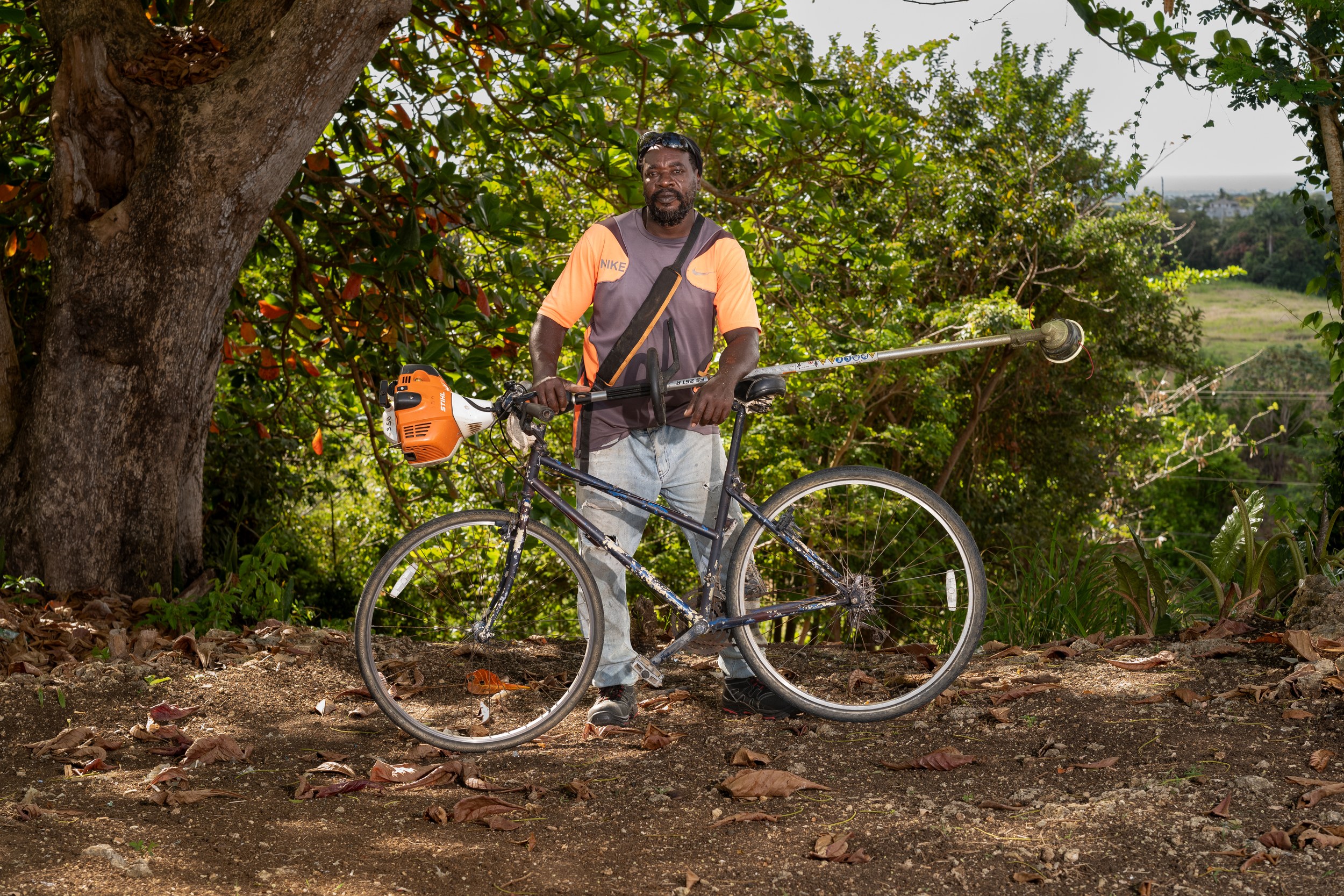 Emerson Lynch with a bicycle and landscaping equipment in Barbados