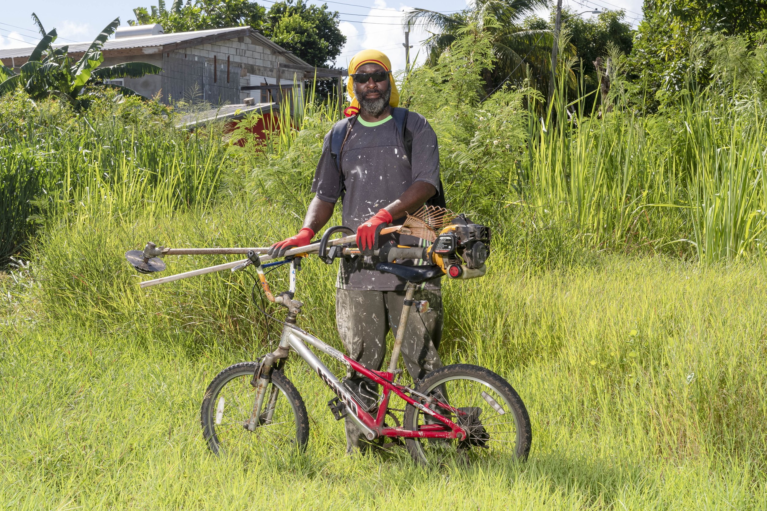 Rodney Burrows with a bicycle and landscaping equipment in Barbados