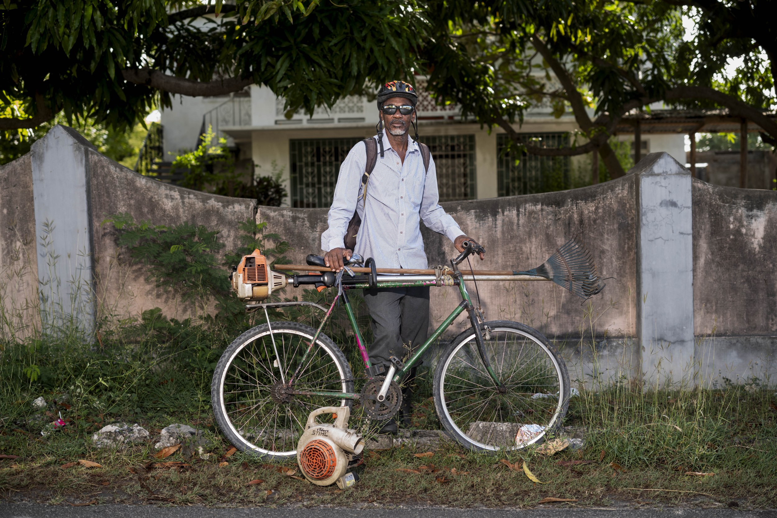 Trevor Braithwaite with a bicycle and landscaping equipment in Barbados