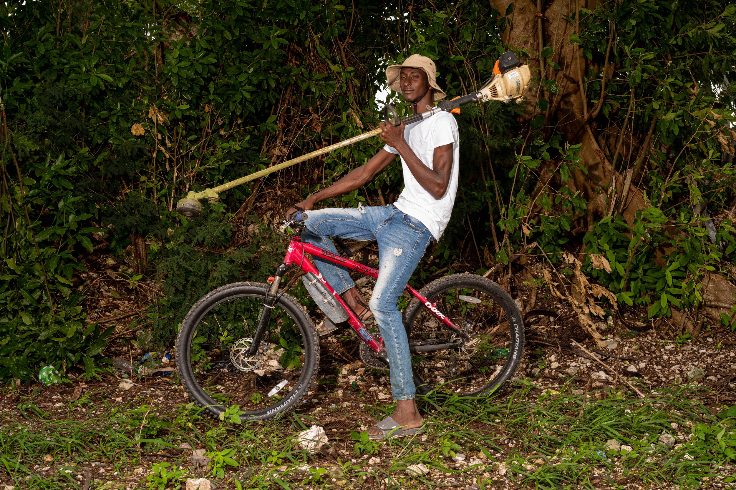 Shaquille Dawn with a bicycle and landscaping equipment in Barbados