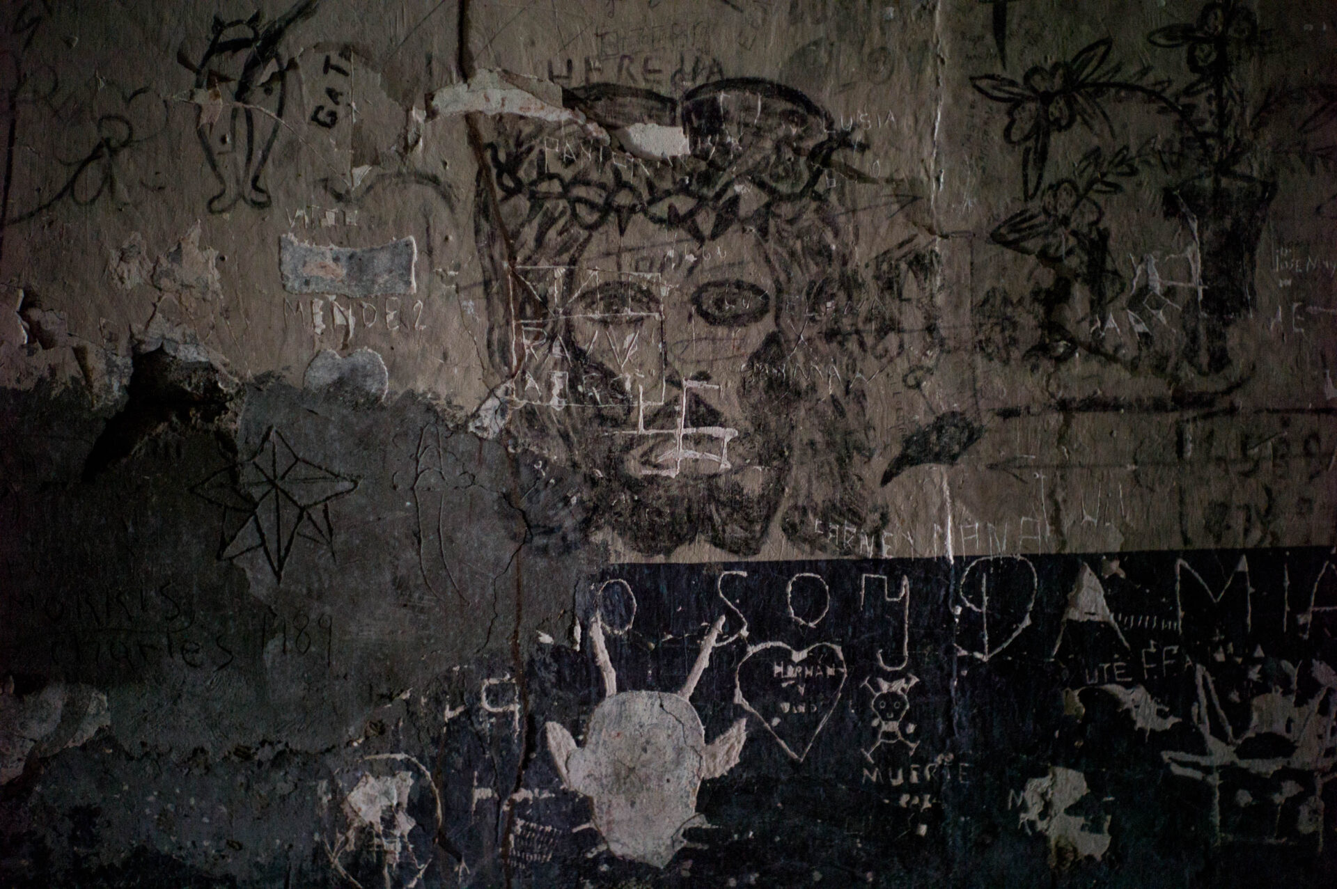 A scarred maximum-security cell wall etched with images of Nazism, Jesus, the devil, and sex