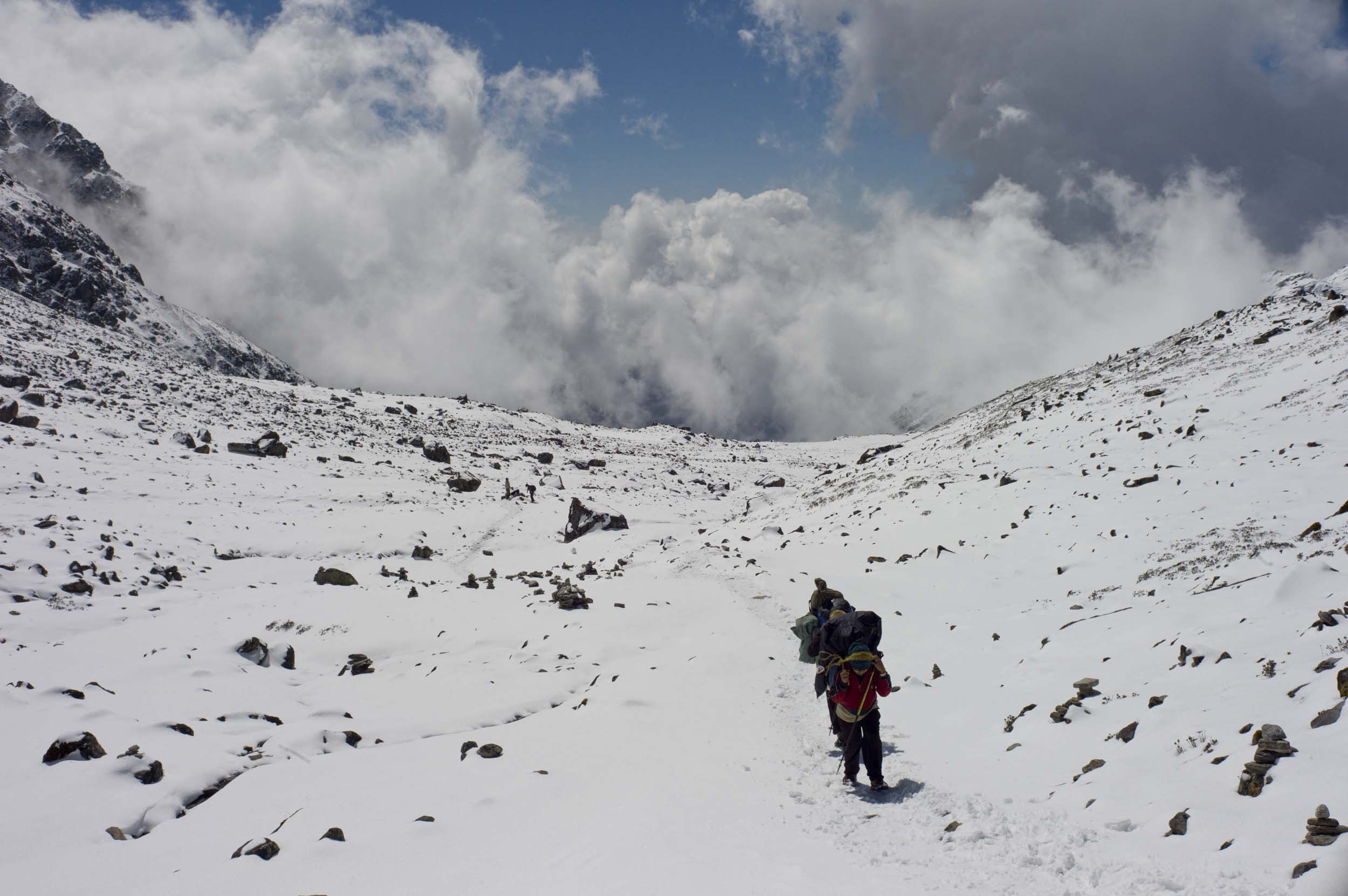 Porters trek up a rock- and snow-covered mountainside connecting Gosain Kund to Ghopte